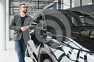 Making his choice. Horizontal portrait of a young man in a suit looking at the car and thinking if he should buy it