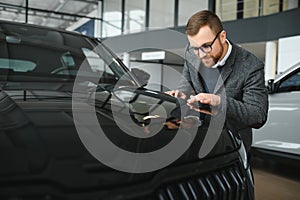 Making his choice. Horizontal portrait of a young man in a suit looking at the car and thinking if he should buy it