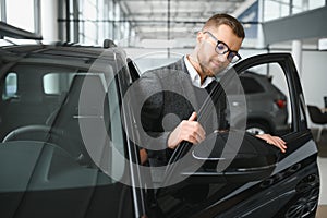 Making his choice. Horizontal portrait of a young man in a suit looking at the car and thinking if he should buy it