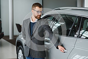 Making his choice. Horizontal portrait of a young man in a suit looking at the car and thinking if he should buy it