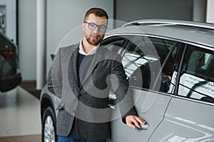 Making his choice. Horizontal portrait of a young man in a suit looking at the car and thinking if he should buy it