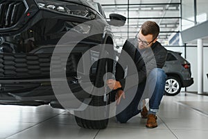Making his choice. Horizontal portrait of a young man in a suit looking at the car and thinking if he should buy it