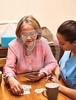 Making memories in their time together. a senior woman playing cards with her caregiver.