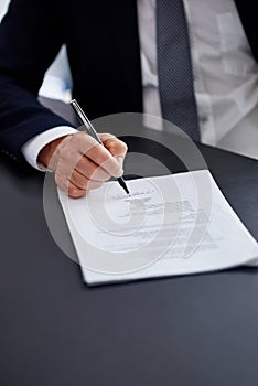 Making mergers happen. Closeup shot of a businessman signing a contract while sitting at a desk in an office.