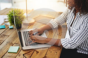 Making money is not that hard anymore. Cropped shot of a woman using her laptop on a wooden table.