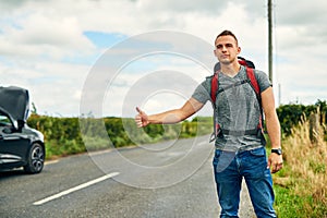 Making a move instead of being left stranded. a young man hitchhiking after having troubles with his car on the road.