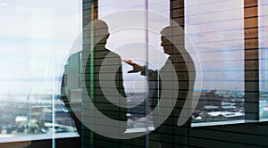 Making moves together. Silhouette shot of two businesspeople having a discussion inside an office building.