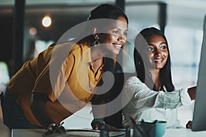 Making it one productive evening. two young businesswomen working together on a computer in an office at night.