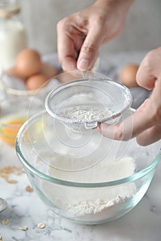 Making pancakes, cake, baking of baker hands sifting flour in bowl. Concept of Cooking ingredients and method on white marble