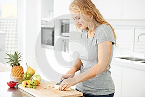 Making the perfect fruit salad. Attractive curvaceous young woman chopping fruit in her kitchen.