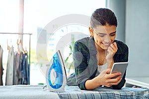 Making plans now that the cleanings done. an attractive young woman using her cellphone while doing the ironing at home.