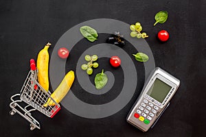 Making purchase online with bank machine, mini trolley and products on black desk background top view