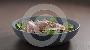 making salad, pumpkin seeds fall over turkey on frisee lettuce in blue bowl on wood table