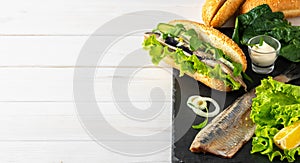 Making a sandwich of herring fillet with onions, cucumber and salad on a stone board. White wooden background with copy space.