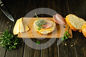 Making a sandwich on a kitchen board. Cheese and bread with sausage on the kitchen table for preparing a quick meal with spices