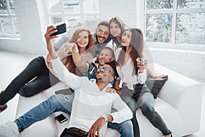 Making selfie. Cheerful young friends having fun and drinking in the white interior