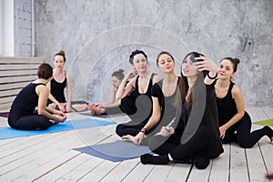 Making selfie. Group of girls in fitness class at the break looking at cell phone, happy and smiling, show funny face