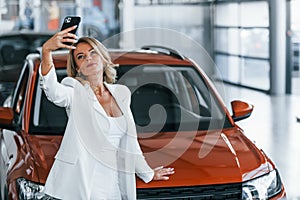 Making selfie. Woman in formal clothes is indoors in the autosalon