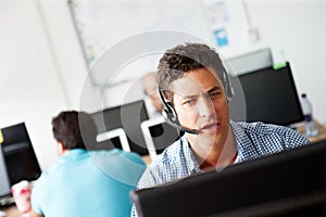 Making sense of the data. A handsome young sales assistant talking on his headset while working on a computer and