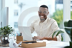 Making some updates to his files. Portrait of a young businessman working on a laptop in an office.