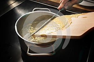 Making spaetzle, homemade egg pasta dough is scrapped from a wooden board into boiling water, typical dish in Schwaben, southern