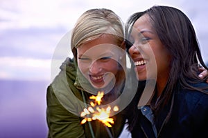 Making special holiday memories. Two young women standing with sparklers with the twilight sky behind them.
