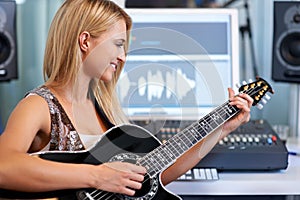 Making the strings sing. A beautiful blonde woman playing her guitar in a recording studio.