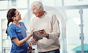 Making sure hes aware of the ins and outs. a young female nurse and her senior patient looking at a tablet in the old