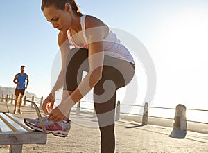 Making sure theyre secure. an athletic woman tying her shoe laces on a bench.