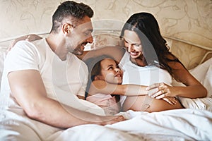 Making sure the unborn baby gets love too. a happy little girl lying in bed with her dad and pregnant mother.