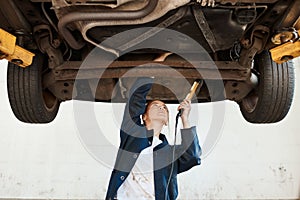 Making sure your car is in good condition and running smoothly and safely. a female mechanic working under a lifted car.