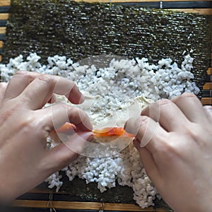 Making Sushi Rolls at Home: Female Hands Put Salmon Fish Strips on Cream Cheese, Rice and Nori Seaweed Sheet Placed on a Bamboo