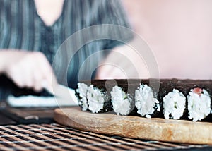 Making Sushi Rolls at Home: Rolls Sealing On the Wooden Board before Slicing. Blurred Woman Hands Spreading Rice across the Nori