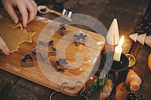 Making traditional christmas gingerbread cookies on rustic table with candle, spice, decorations. Moody image. Hand cutting