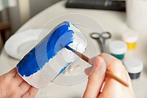 Coloring papier mache. Making utensils from paper mache. The child paints with a brush a blank of paper in the shape of a glass