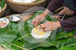 Making wrapping Chung Cake, the Vietnamese lunar new year Tet food outdoor with old woman hands and ingredients. Closed-up.