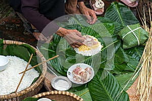 Making wrapping Chung Cake, the Vietnamese lunar new year Tet food outdoor with old woman hands and ingredients. Closed-up.