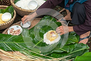 Making wrapping Chung Cake, the Vietnamese lunar new year Tet food outdoor with old woman hands and ingredients. Closed-up