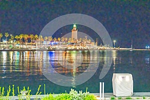 Malaga lighthouse from port promenade at night