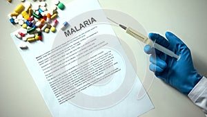 Malaria word typed on paper, doctor hand with syringe pills and tablets on table
