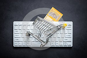 Malay banknotes, White computer keyboard, Miniature shopping cart, Black background, Online shopping concept in stores, Low prices