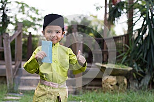 A Malay boy in Malay traditional cloth showing his happy reaction after received money pocket during Eid Fitri or Hari Raya celebr