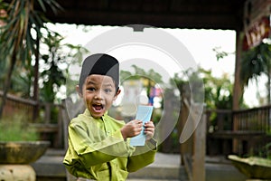 A Malay boy in Malay traditional cloth showing his happy reaction after received money pocket during Eid Fitri or Hari Raya celebr