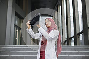 Malay lady doctor radiologist, looking at Xray results, standing outdoors