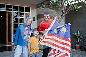 Malaysian family holding malaysia flag in front of their house