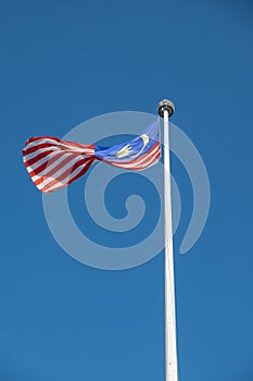 Malaysian national flag flying in wind on a pole with blue sky