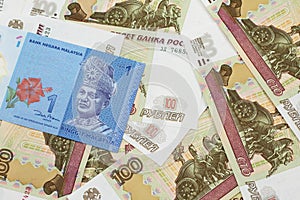 A Malaysian ringgit on a background of Russian one hundred ruble bills