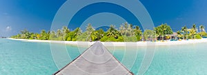 Maldives island beach panorama. Palm tree and beach bar and long wooden pier pathway. Tropical vacation and summer holiday concept