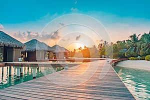 Maldives resort island villas, bungalows in sunset with wooden jetty, amazing colorful sky. Perfect sunset beach, summer vacation