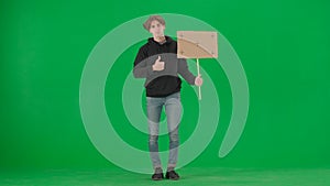 A male activist holds a blank poster and shows a thumbs up. A young man in casual clothes holds a placard on a green